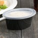 A black Pactiv Ellipso souffle container with a clear lid.