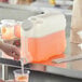 A woman pouring an orange and white drink into a Choice plastic beverage container.