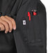 A woman's hand holding a red pen in the pocket of a black Uncommon Chef Napa long sleeve chef coat.