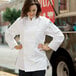 A woman in a white Uncommon Chef long sleeve chef coat standing in a professional kitchen.