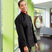 A woman wearing a black Uncommon Chef long sleeve chef coat with side vents.