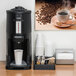 A Zojirushi stainless steel thermal beverage dispenser on a table with cups of coffee.