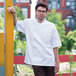A man wearing an Uncommon Chef white short sleeve chef coat with a mesh back.