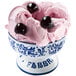 A white bowl of pink ice cream with black cherries on top.