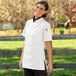 A woman wearing a white Uncommon Chef short sleeve chef coat with side vents.