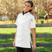 A woman wearing a Uncommon Chef white short sleeve chef coat.