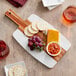 An Acopa acacia wood and marble serving board with cheese, crackers, and grapes.