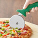A hand using a Choice 4" Pizza Cutter with a green handle to cut a pizza.