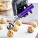 A close-up of a purple metal scoop filled with cookie dough.