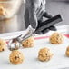 A person in black gloves using a black Choice #30 Thumb Press Disher to scoop cookie dough.