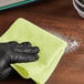 A hand in a black glove wiping a surface with a yellow Lavex microfiber cloth.