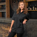 A woman wearing a black Mercer Culinary short sleeve brewer shirt leaning on a bar counter.