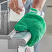 A person wearing a green Lavex Microfiber mitt while cleaning a sink.