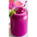A jar of organic Pitaya Foods dragon fruit smoothie with a purple and white striped straw.