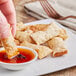 A hand dipping a Handy Thai Chili Shrimp Roll into a bowl of sauce.