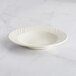 An ivory stoneware bowl with an embossed rim on a white table.