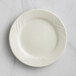 An Acopa Swell ivory stoneware plate with a curved, embossed edge.