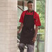 A man in a black and red pinstripe Uncommon Chef butcher apron standing in a professional kitchen.