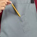 A person putting a pencil in the pocket of a gray Uncommon Chef Surge bib apron.