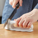 A person's hand using the Kai Serrated Handheld Knife Sharpener to sharpen a knife.
