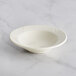 An Acopa Swell ivory stoneware bowl with an embossed wide rim on a marble surface.