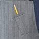 A pencil in a pocket of a grey denim bib apron.