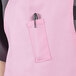 A person wearing a pink Uncommon Chef bib apron with a pen in the pocket.