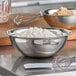 A Vollrath stainless steel mixing bowl filled with flour on a table with a whisk.