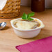 A Tuxton eggshell china French onion soup bowl filled with soup topped with cheese and a leaf.