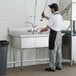 A man washing dishes in a Steelton 3 compartment sink in a commercial kitchen.
