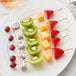 A fruit skewer with kiwi, strawberries, and grapes on a Royal Paper bamboo skewer.