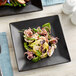 A plate of food with octopus salad on a matte black square stoneware plate.