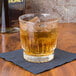 A Libbey Winchester old fashioned glass of whiskey with ice on a black napkin.