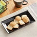 A glossy black rectangular Acopa stoneware platter with cookies and a cup of coffee on it.