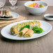 A blue oval Thunder Group melamine platter with sushi and other food on a table.