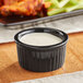 An Acopa glossy black fluted stoneware ramekin filled with white sauce.