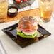 A sandwich on an Acopa glossy black square stoneware plate with a toothpick.
