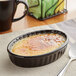 An oval black Acopa Creme Brulee dish filled with creme brulee on a table.