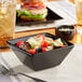 A bowl of salad with lettuce and tomatoes in a black Acopa stoneware bowl on a table.