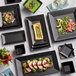 A table with Acopa matte black square stoneware bowls of food.