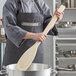A person in a chef's uniform using an American Metalcraft wood paddle.