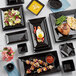 A table with Acopa glossy black square stoneware plates of food.