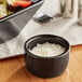A close-up of a glossy black Acopa stoneware ramekin filled with shredded white cheese.
