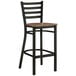A Lancaster Table & Seating black finish Ladder Back Bar Stool with a vintage wood seat.