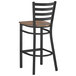 A Lancaster Table & Seating black finish ladder back bar stool with a vintage wood seat.