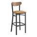A Lancaster Table & Seating black bar stool with a light brown vinyl seat and vintage wood back.
