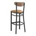 A black Lancaster Table & Seating bar stool with a light brown cushioned seat and vintage wood back.