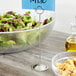 A bowl of salad with a stainless steel menu holder with a blue and white label.
