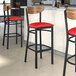 Three Lancaster Table & Seating black bar stools with red vinyl seats and vintage wood backs.