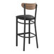 A Lancaster Table & Seating black wood bar stool with a black cushioned seat and vintage wood back.